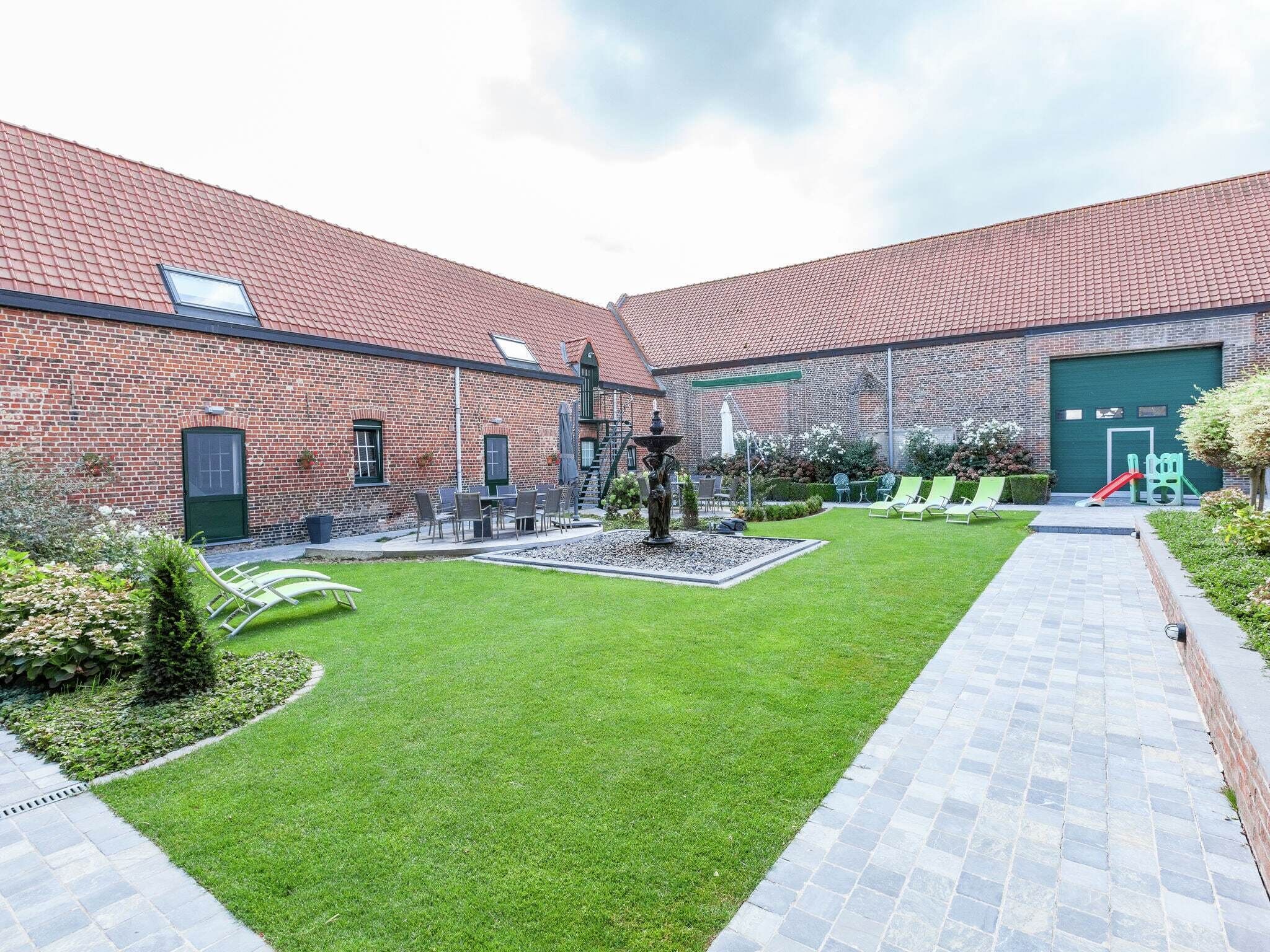 A courtyard with a brick building, a green lawn, outdoor seating, and a children's play area.