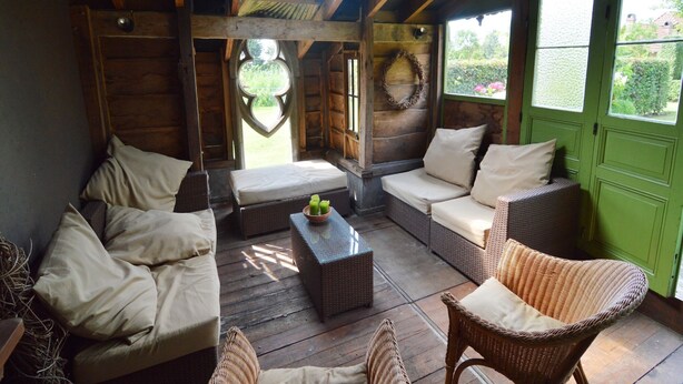 A cozy room with wooden walls, a green door, and a skylight. There are wicker sofas and a small table with a bowl of fruit. - Comfortable Home with Sauna (Vloesberg (flobecq))