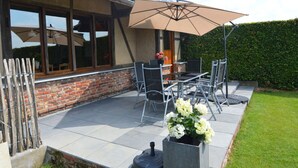 A patio with a table and chairs, a large umbrella, and a flower planter. - Comfortable Home with Sauna (Vloesberg (flobecq))