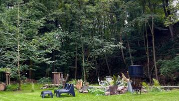 Een weelderige tuin met verschillende bomen, een klein vijvertje en tuinmeubilair.