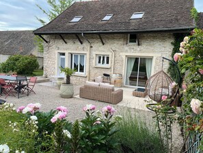 A stone house with a patio, outdoor seating, and a garden with flowers. - Gîte de Charme Capacité 10 Personnes (Allériot)