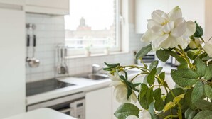 A modern kitchen with white cabinets, a window, and a plant with white flowers.