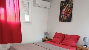 Une chambre à coucher avec un lit, une table de chevet, un climatiseur, une fenêtre avec un rideau et un tableau au mur.
