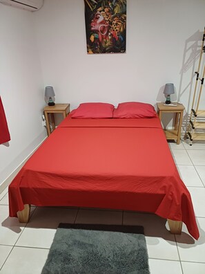 Un lit bien fait, avec une literie rouge, deux tables de chevet avec des lampes, un tableau au mur et un tapis bleu sur le sol.