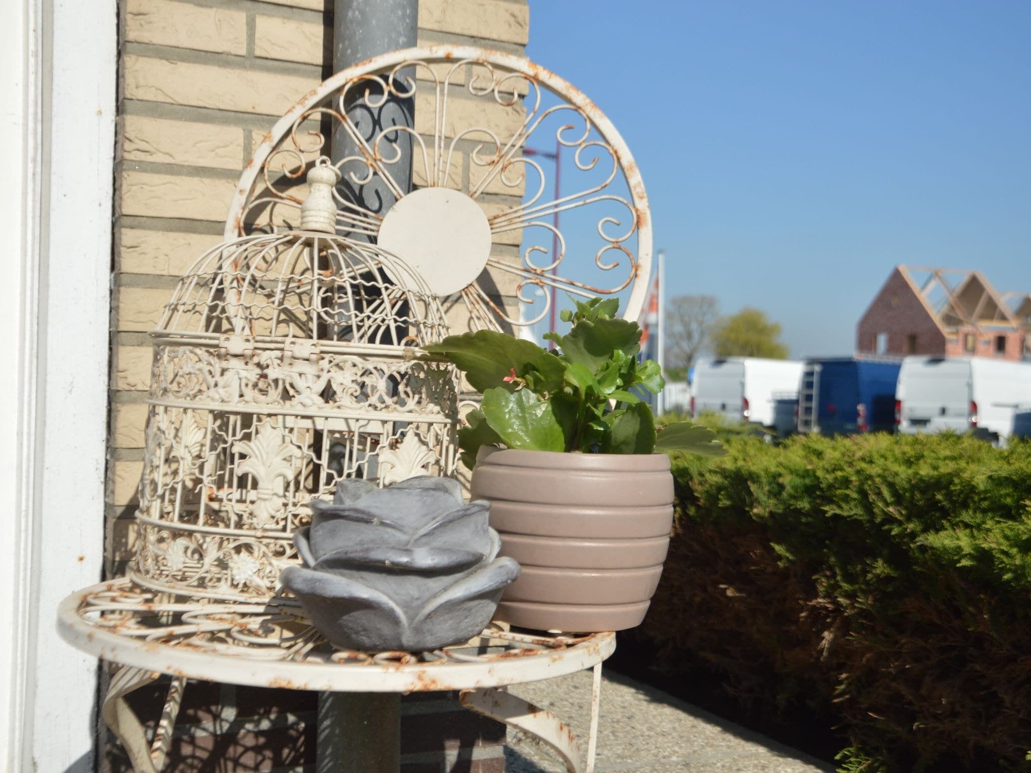 A metal birdcage with a potted plant and a decorative stone on a metal stand.