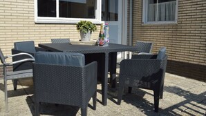 Un patio exterior con una mesa y sillas, una planta en maceta y una botella de champán.