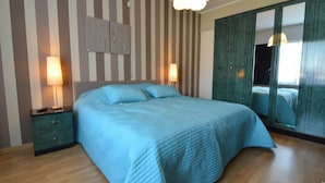 Un dormitorio con una cama grande, papel tapiz a rayas, una mesita de noche con lámpara y un armario con espejo.