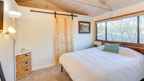 Un dormitorio con cama, techo de madera, ventana y lámpara de pared.