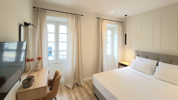 A hotel room with a bed, a desk with a chair, a TV, and two windows with curtains. - Lorenzo Mavili Suite (Corfu)
