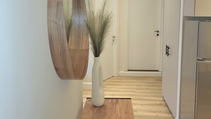 A hallway with a wooden floor, a white vase with dried plants, a wooden-framed mirror, and a stainless steel refrigerator. - Lorenzo Mavili Suite (Corfu)