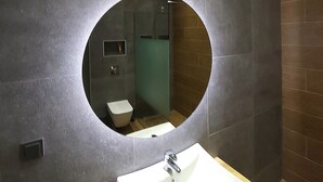 A bathroom with a round mirror, a white sink, and a toilet. - Lorenzo Mavili Suite (Corfu)