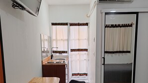 A compact hotel room with a wooden desk, a black chair, a bed, a TV, a small kitchenette, and a sliding door leading to a balcony. - CASA COCO OAXACA (Oaxaca)