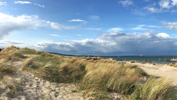 Un paisaje costero con dunas, un faro y un muelle que se adentra en el mar.