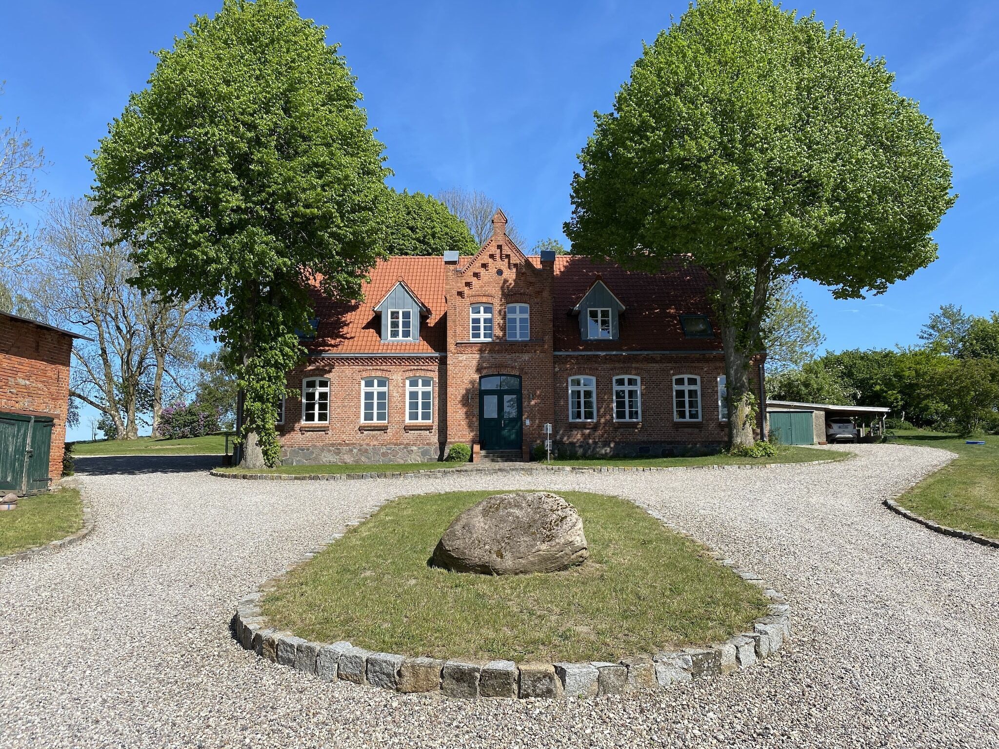 Une maison traditionnelle en briques, avec une allée en gravier et un grand rocher au centre.