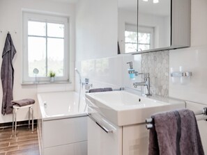 A modern bathroom with a large white sink, a mirror, and a shower. - Landurlaub in Lübberstorf (Lübberstorf)