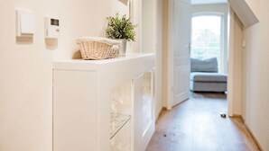Un pasillo con una pared blanca, una cesta con una planta y una estantería de cristal con vasos.
