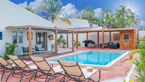 A poolside area with lounge chairs, a barbecue, and a covered seating area.