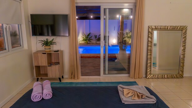 A room with a bed, a TV, a sliding glass door to a pool, a wooden cabinet, and a large mirror.