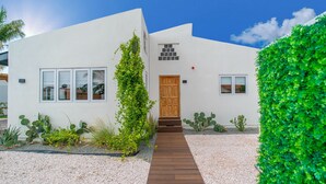 A modern house with a wooden door, white exterior, and a gravel pathway leading to the entrance.