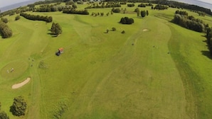 Ein Luftbild eines Golfplatzes mit mehreren Bahnen, Sandfängen und Bäumen.