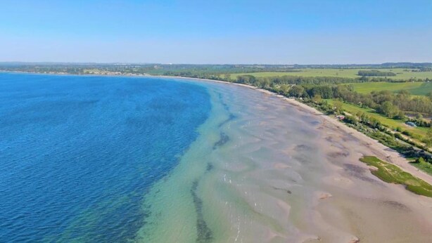Eine Küstenlandschaft mit blauem Meer, Sandstrand und grünen Feldern.