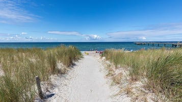 Un sentier de sable qui longe la plage et mène à l’océan, avec une jetée en arrière-plan.