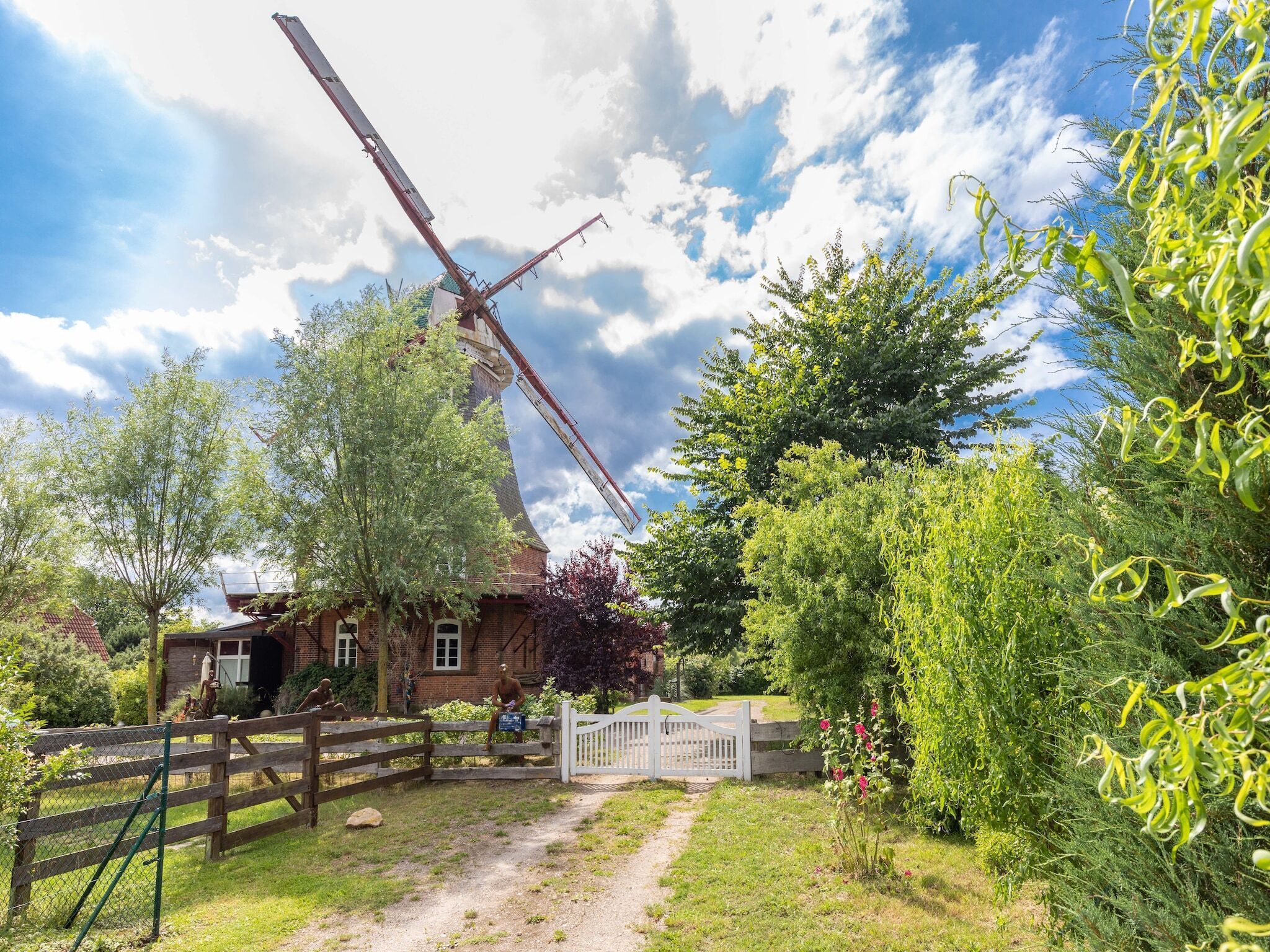 Un moulin à vent traditionnel, avec une clôture en bois et un chemin menant à un portail blanc.