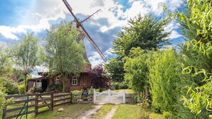 Un moulin à vent traditionnel, avec une clôture en bois et un chemin menant à un portail blanc.