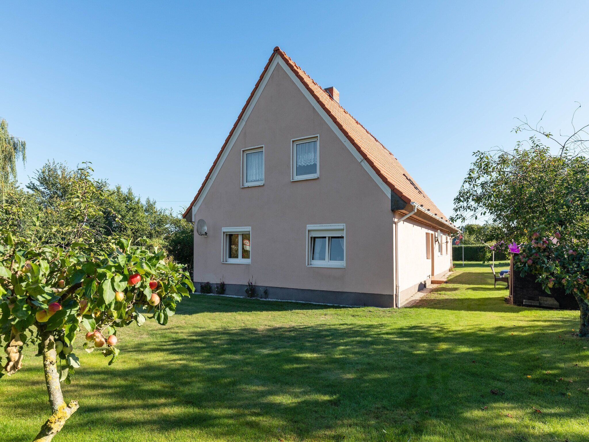 Ein zweistöckiges Haus mit einem geneigten Dach, einem gepflegten Rasen und Obstbäumen im Vordergrund.