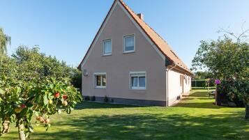 Ein zweistöckiges Haus mit einem geneigten Dach, einem gepflegten Rasen und Obstbäumen im Vordergrund.