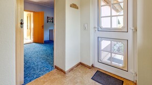 Un couloir avec une porte en bois qui donne sur une pièce dotée d’une moquette bleue et d’un petit réfrigérateur.