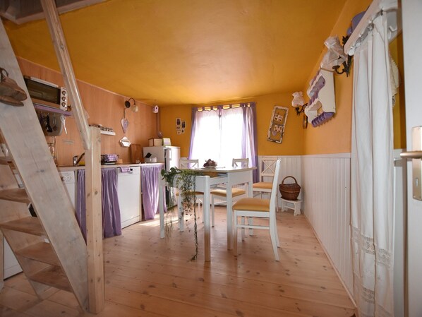 Eine gemütliche Küche mit Holzböden, einem Essbereich mit weißem Tisch und Stühlen und einem Fenster mit violetten Vorhängen.
