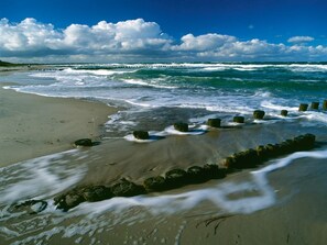 A beach with waves crashing onto the shore, a wooden groyne, and a clear sky. - Gemütliche Ferienwohnung mit Garten in Robertsdorf (Blowatz)