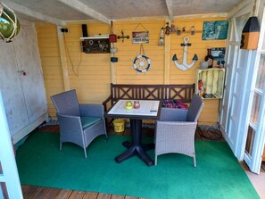 Une pièce d’angle avec un banc en bois et deux chaises en osier disposées autour d’une table recouverte d’un tapis vert.
