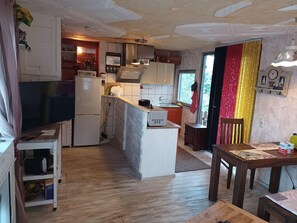 Eine kompakte Küche mit Kühlschrank, Herd und Spüle. Es gibt einen Holzespeisetisch mit Stühlen und eine kleine Kücheninsel ebenfalls mit Spüle.