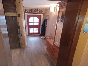 Un pasillo con suelo de madera, una puerta roja con paneles de vidrio y un mueble de madera con cajones.