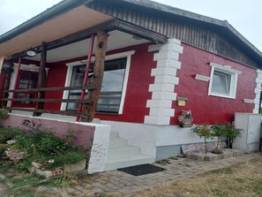 Un edificio rojo y blanco con una escalera de madera que conduce a un porche, un letrero de bienvenida y una pequeña área ajardinada.