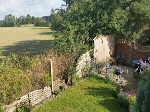 Un jardín con cerco de madera, un cobertizo pequeño y una mesa con sillas.
