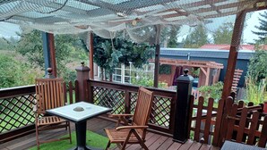 Eine Holzterrasse mit Tisch und Stühlen, umgeben von einem Holzzaun und einer Pergola mit Netzbedachung.