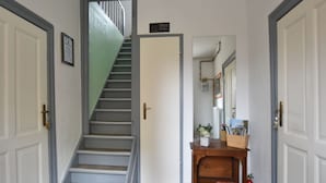 Een hal met een trap, een deur met een bordje, een houten console tafel met tijdschriften en een brandblusser.
