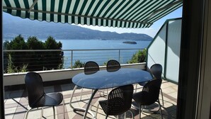 Een terras met een tafel en stoelen, met uitzicht op een meer en bergen.