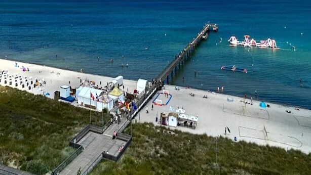 Een strand met een pier die zich uitstrekt in de zee, een zandstrand en enkele boten.