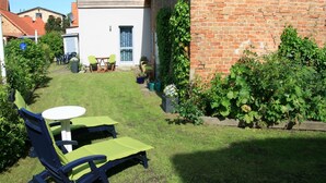 A backyard with a lawn, a table, two lounge chairs, and a brick wall. - Wohnung in Klütz nahe Schloss Bothmer (Klütz)