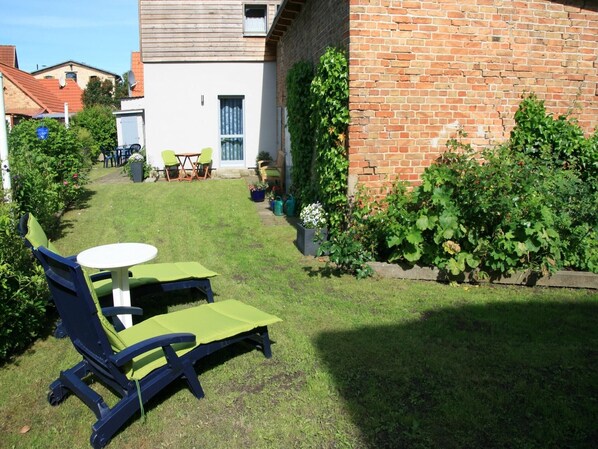 Un jardin avec une pelouse, une table, deux chaises longues et un mur en briques.