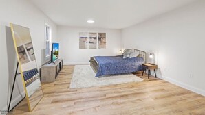 A bedroom with a bed, a bedside table, a lamp, a large mirror, and artwork on the wall.