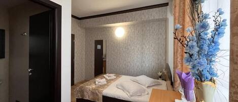 A hotel room with a bed, a wooden desk, and a vase with flowers.