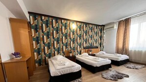 A hotel room with two beds, a wooden floor, a patterned wall, and a window with curtains. - Pensiunea Nys (Iasi)