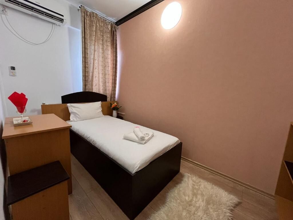 A small, neatly arranged bedroom with a single bed, a bedside table, a lamp, and a wall-mounted air conditioner.