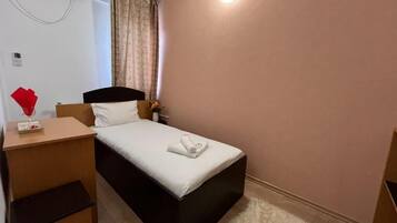 A small, neatly arranged bedroom with a single bed, a bedside table, a lamp, and a wall-mounted air conditioner.