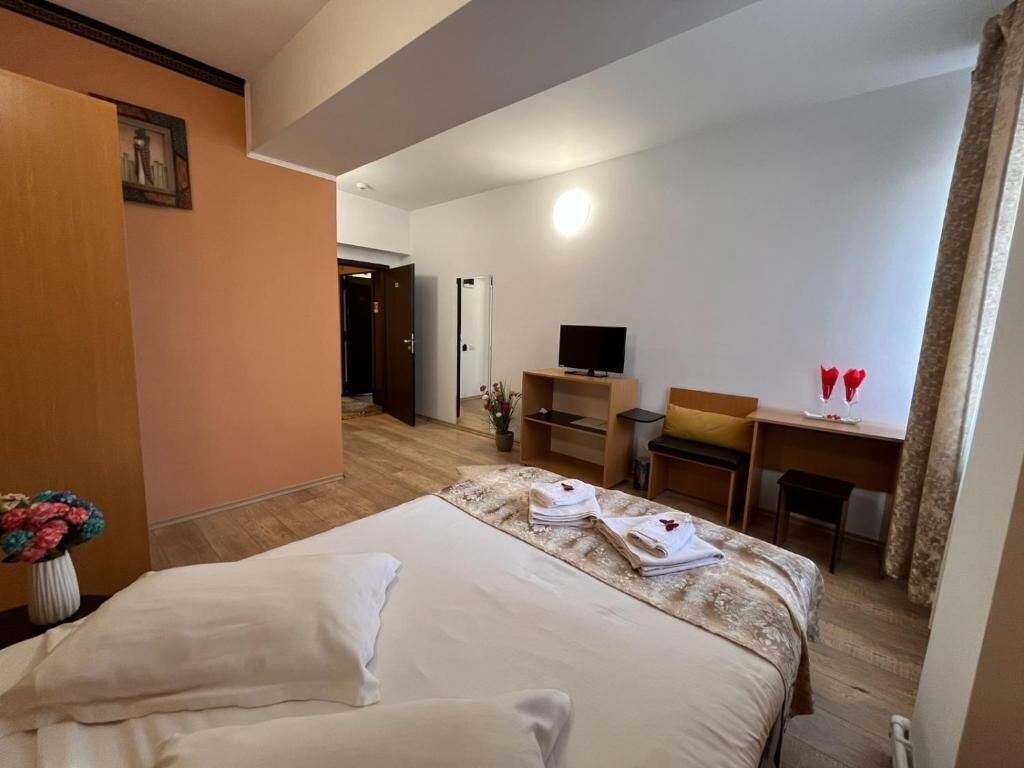 Habitación de hotel con una cama grande, un escritorio con silla, un televisor y una mesita con dos vasos rojos.